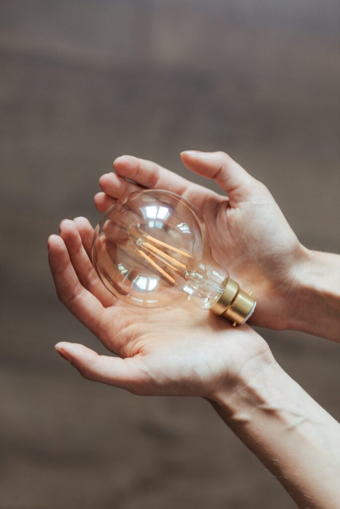 Photo de 2 mains jointes, paumes vers le haut avec une ampoule posée dessus. Le citoyen devient acteur de sa consommation.